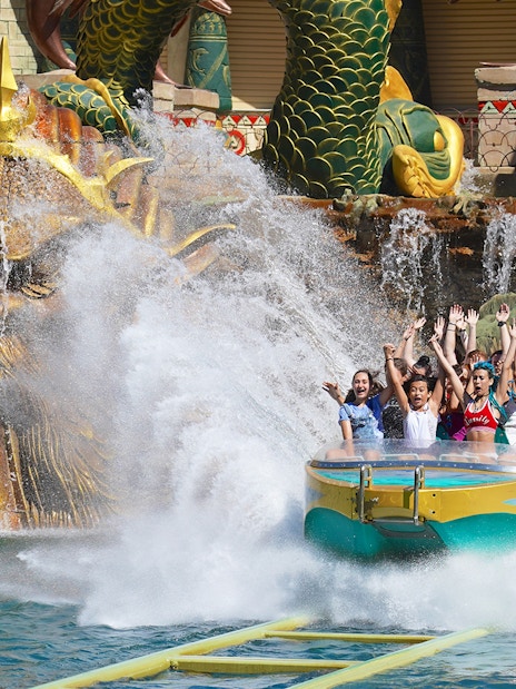 Visitors enjoying a thrilling water ride at Gardaland Park with a dragon sculpture backdrop.