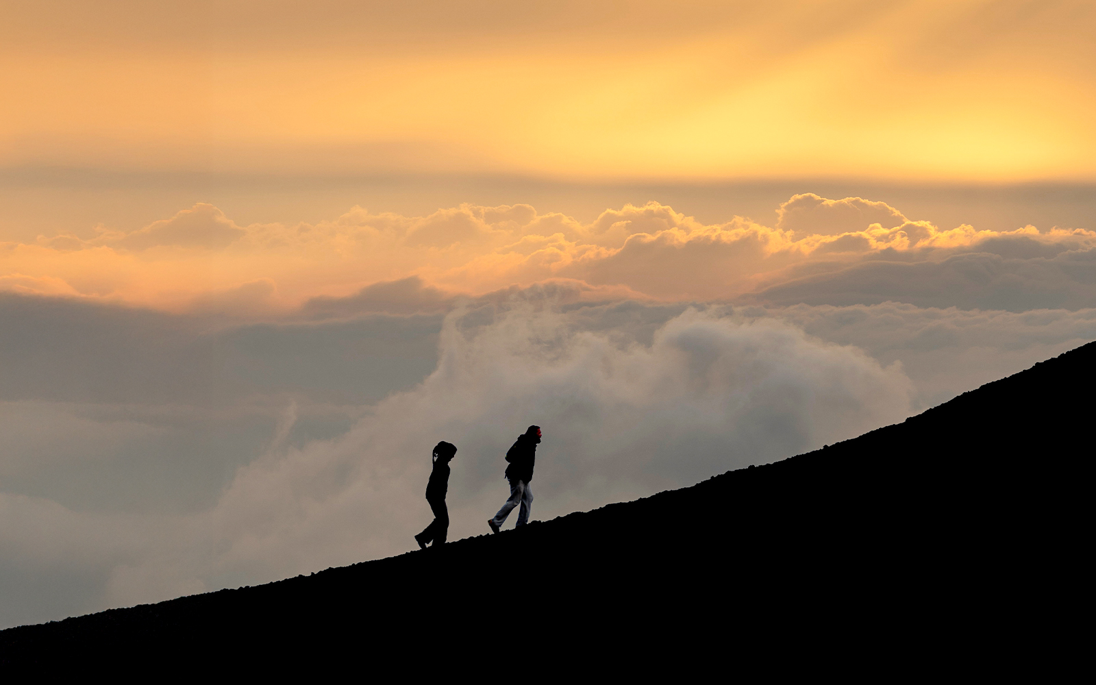 Hikers ascending Mount Etna at sunset with a vibrant sky.