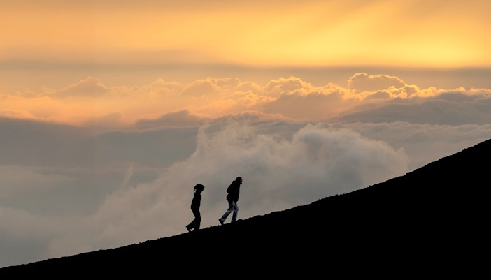 Hikers on Mount Etna at sunset with a view of volcanic landscape.