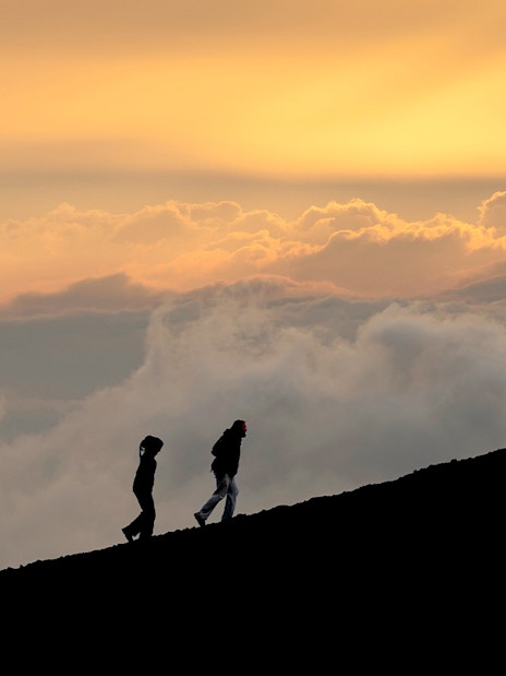 Hikers ascending Mount Etna at sunset with a vibrant sky.