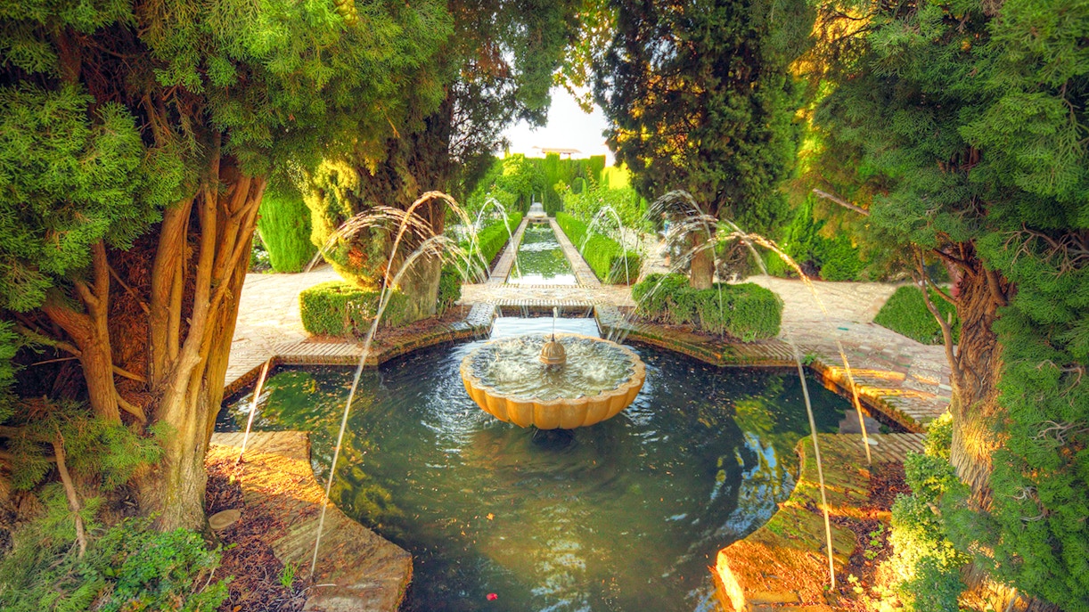 Fountain in Alhambra garden surrounded by trees, Granada, Spain.