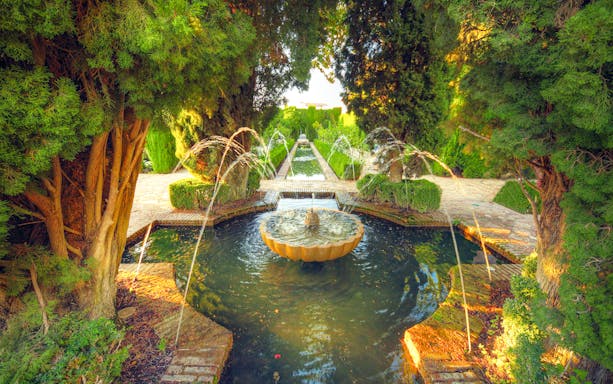 Fountain in Alhambra garden surrounded by trees, Granada, Spain.
