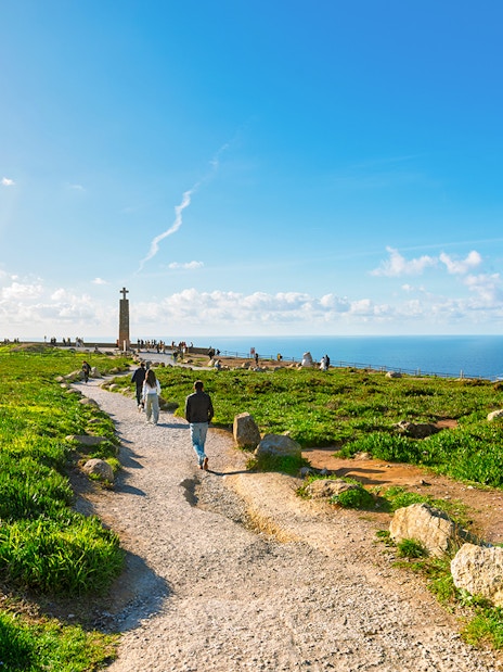 Tourists walking along a path with Atlantic Ocean view at Cabo de Roca, Portugal.