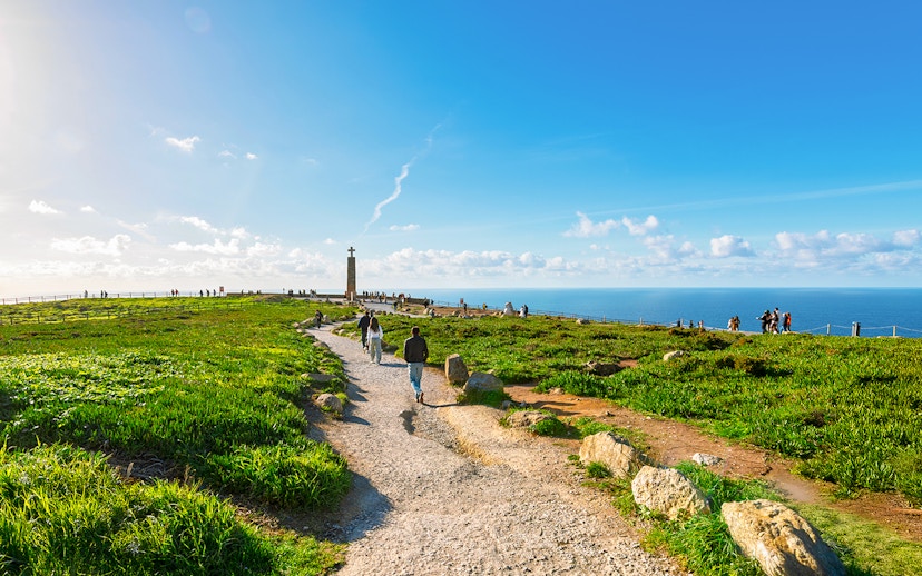 Tourists walking along a path with Atlantic Ocean view at Cabo de Roca, Portugal.