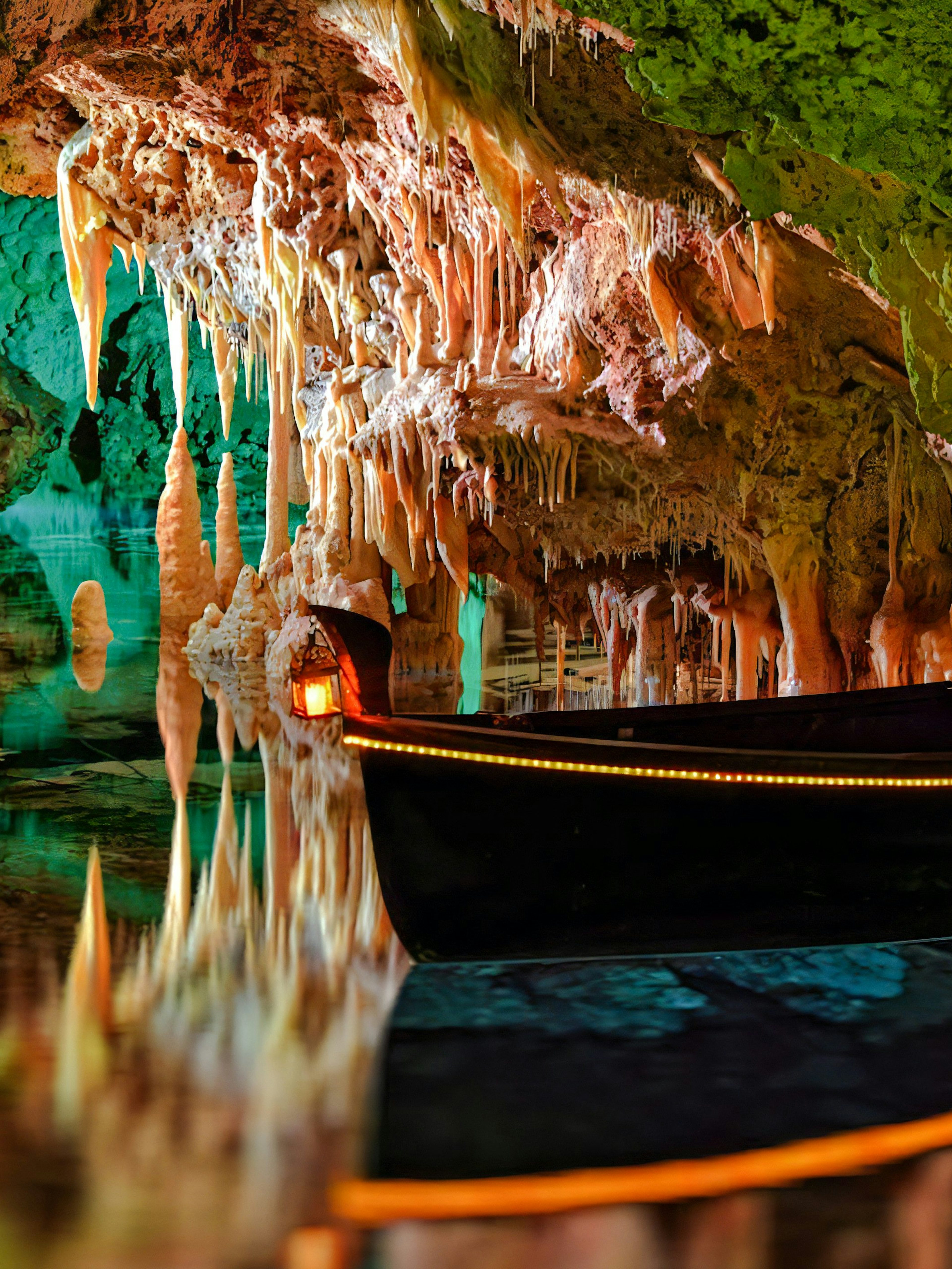 Boat inside Hams Caves with stalactites and colorful lighting, Mallorca.