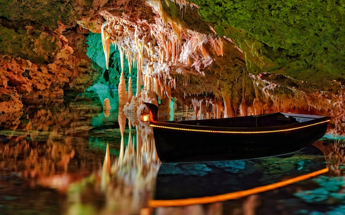 Boat inside Hams Caves with stalactites and colorful lighting, Mallorca.