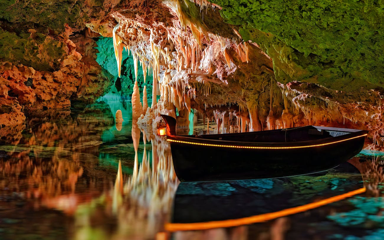 Boat inside Hams Caves with stalactites and colorful lighting, Mallorca.