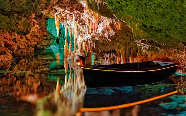 Boat inside Hams Caves with stalactites and colorful lighting, Mallorca.