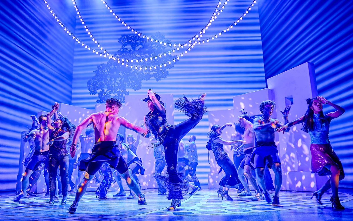 Performers dancing energetically in a vibrant Mamma Mia stage production.