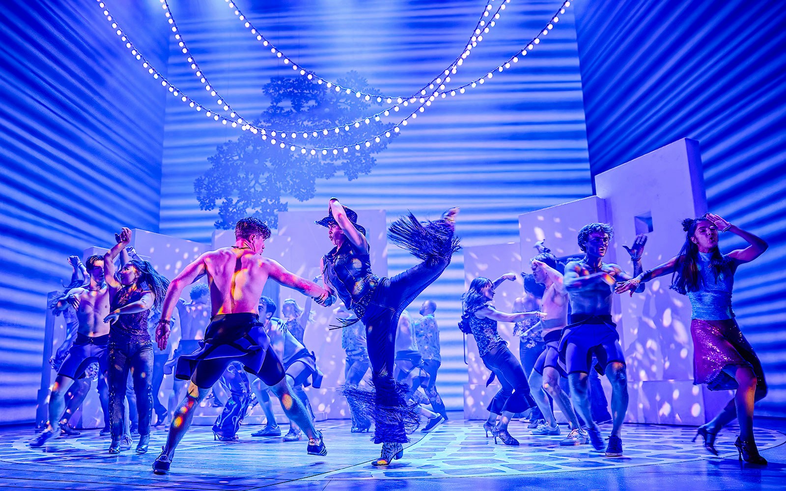 Performers dancing energetically in a vibrant Mamma Mia stage production.