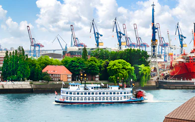 Harbor cruise boat on the Elbe River with cranes in Hamburg, Germany.