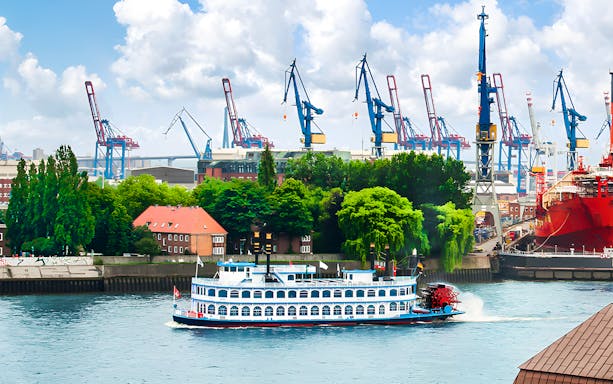 Harbor cruise boat on the Elbe River with cranes in Hamburg, Germany.