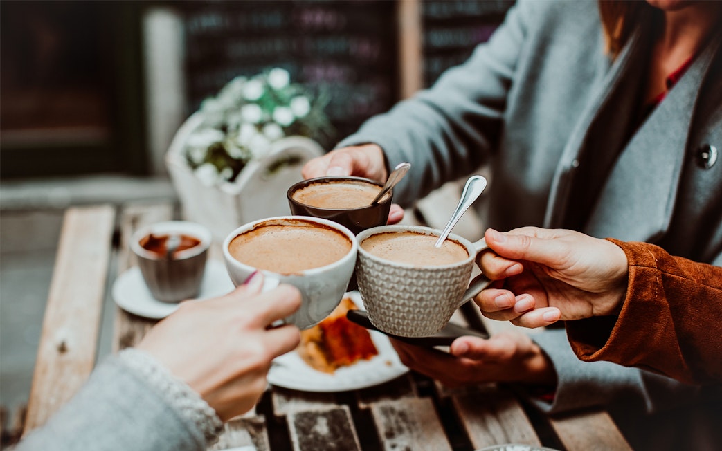 Three people toasting with coffee cups at an outdoor café table.