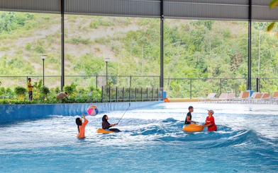 Children enjoying a wave pool with inflatable tubes and a beach ball.