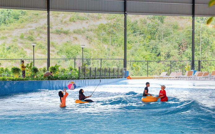Children enjoying a wave pool with inflatable tubes and a beach ball.