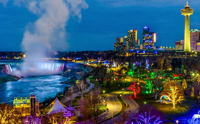 Niagara Falls illuminated at night during the Festival of Lights with city skyline.