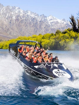 Jet boat with tourists on Lake Wakatipu, Queenstown, with Remarkables mountain range in background.
