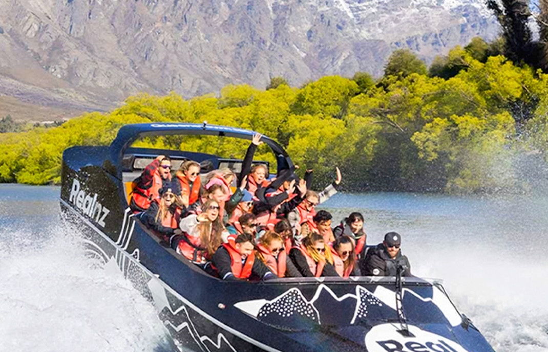 Jet boat with tourists on Lake Wakatipu, Queenstown, with Remarkables mountain range in background.