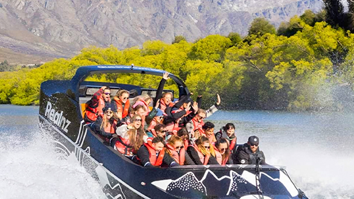 Jet boat with tourists on Lake Wakatipu, Queenstown, with Remarkables mountain range in background.