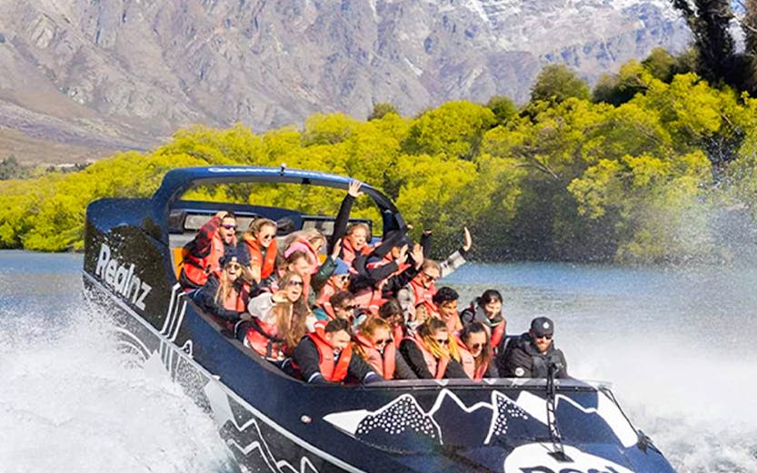 Jet boat with tourists on Lake Wakatipu, Queenstown, with Remarkables mountain range in background.