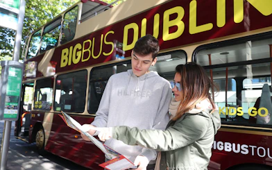Tourists reading a map beside a Dublin hop-on-hop-off bus.