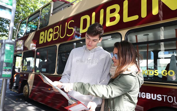 Tourists reading a map beside a Dublin hop-on-hop-off bus.