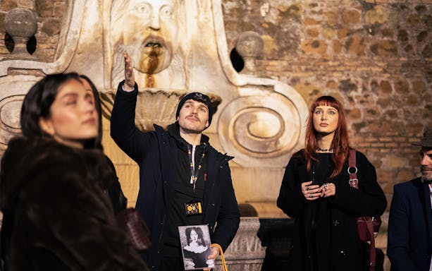 Local guide leading a haunted ghosts tour in Rome, gesturing near a historic stone fountain.