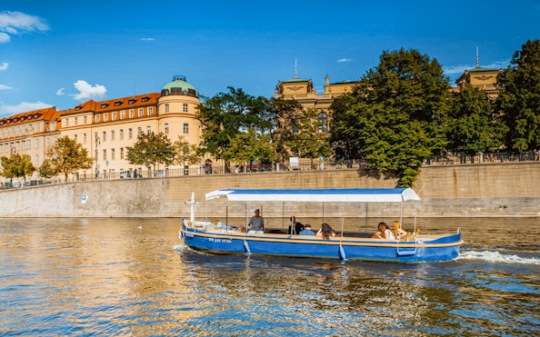 Sightseeing cruise boat on Devils Channel in Prague with historic buildings in the background.