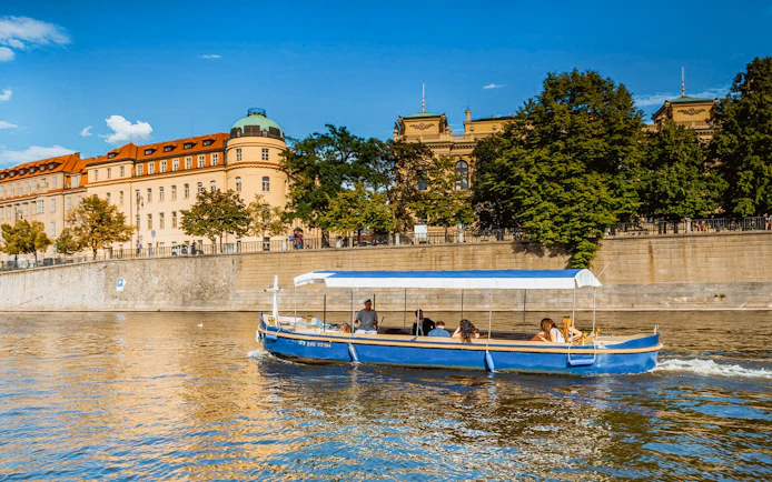 Sightseeing cruise boat on Devils Channel in Prague with historic buildings in the background.
