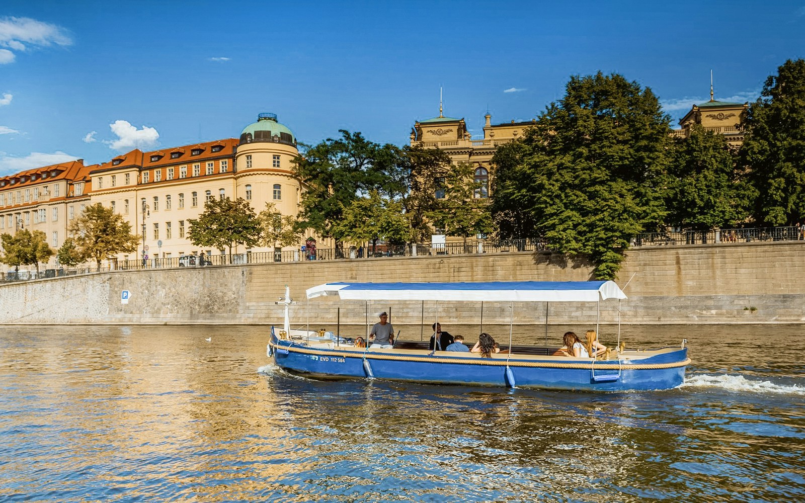 Sightseeing cruise boat navigating Devils Channel in Prague with historic buildings in the background.