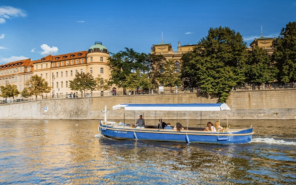 Sightseeing cruise boat on Devils Channel in Prague with historic buildings in the background.