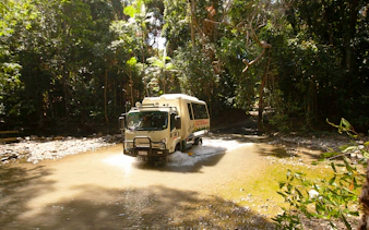 Tour bus crossing a stream in Daintree Rainforest, part of the 2-day Great Barrier Reef tour from Cairns.