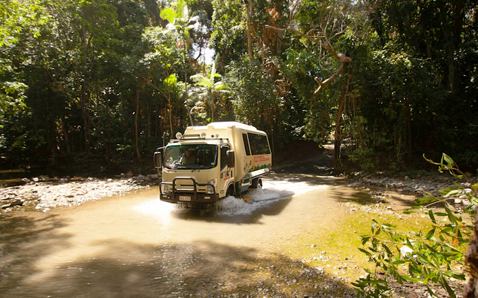 Tour bus crossing a stream in Daintree Rainforest, part of the 2-day Great Barrier Reef tour from Cairns.