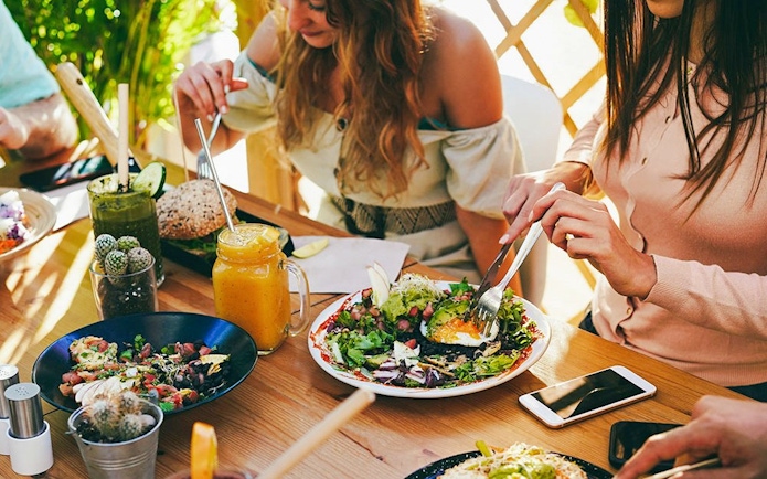 Friends enjoying brunch with fresh salads and drinks at an outdoor cafe.