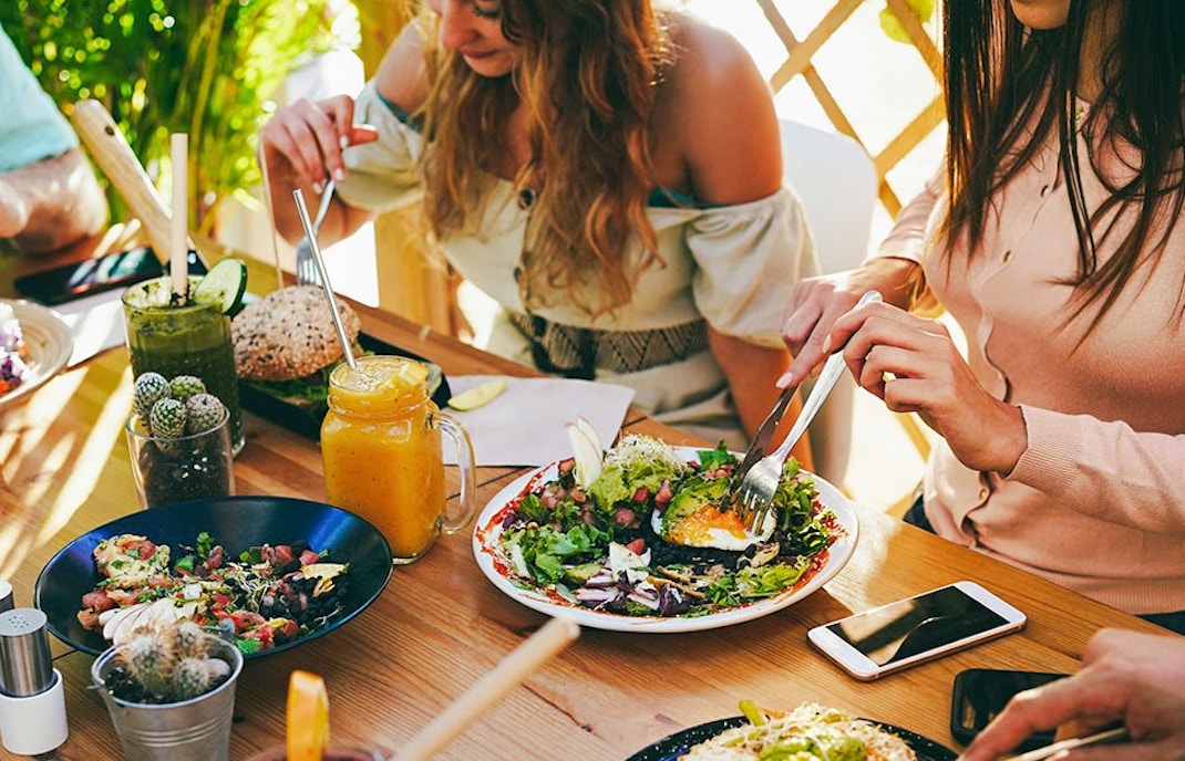 Friends enjoying brunch with fresh salads and drinks at an outdoor cafe.