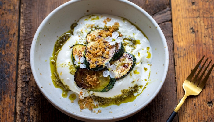 Burrata with pesto, grilled courgettes, crispy garlic breadcrumbs, and radish flowers in a bowl.