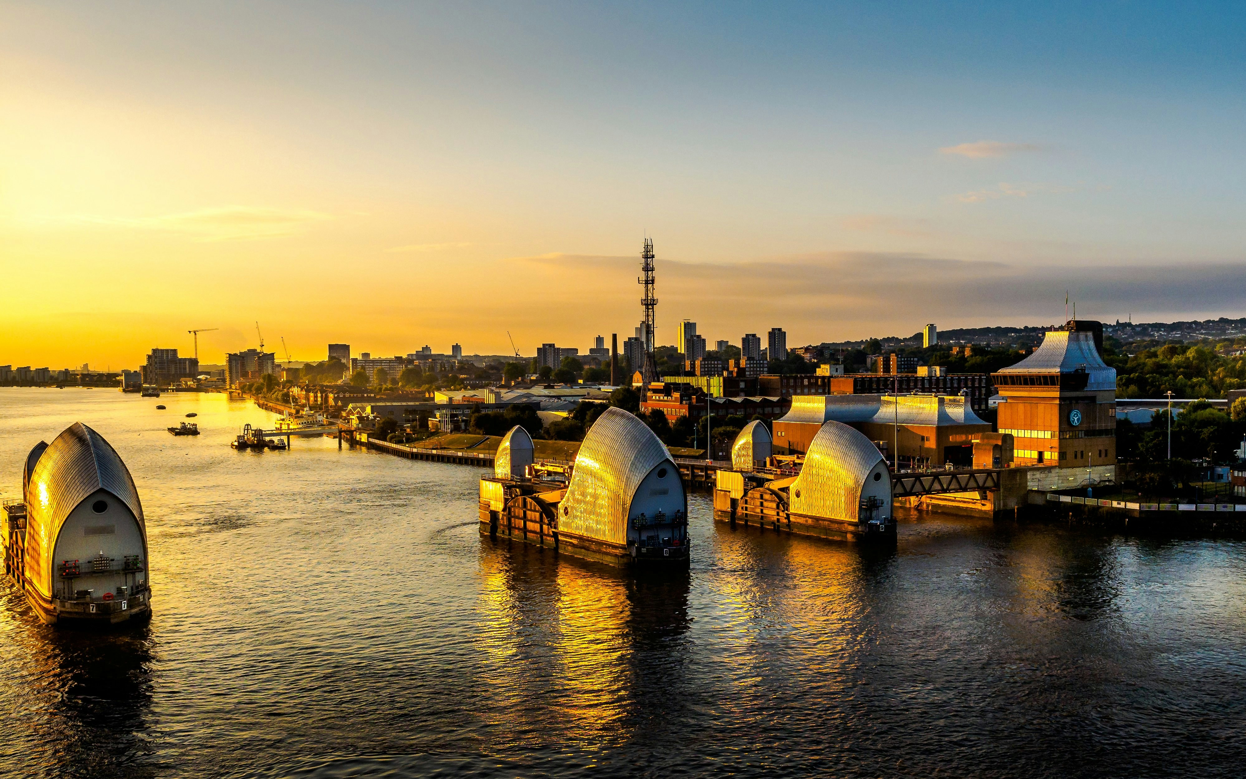 Thames Barrier at sunset in London with city skyline in the background.