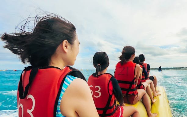 Group enjoying a banana boat ride on the ocean, wearing life jackets.