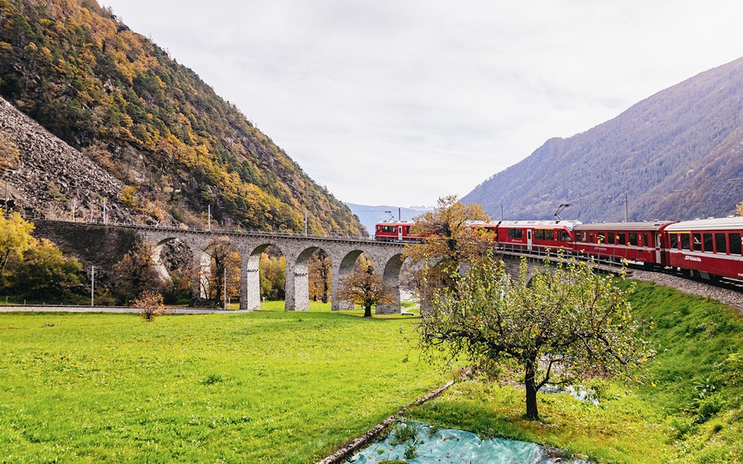 Bernina Red Train crossing a stone viaduct in a scenic valley near St. Moritz.