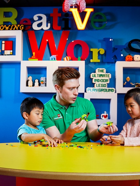Children building LEGO models with instructor at LEGOLAND Discovery Centre.