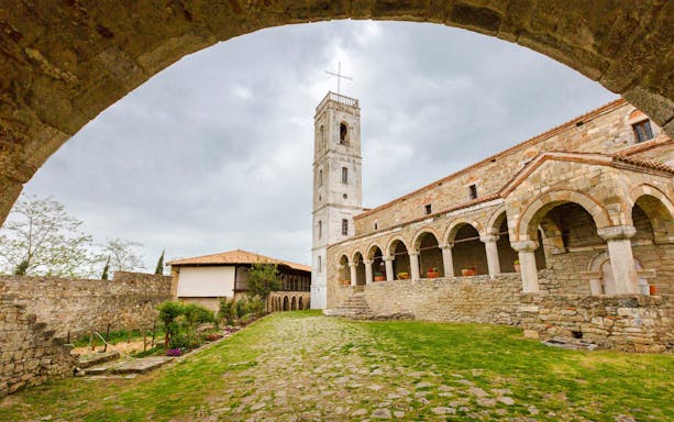 Church of Ardenica courtyard with stone arches and bell tower.