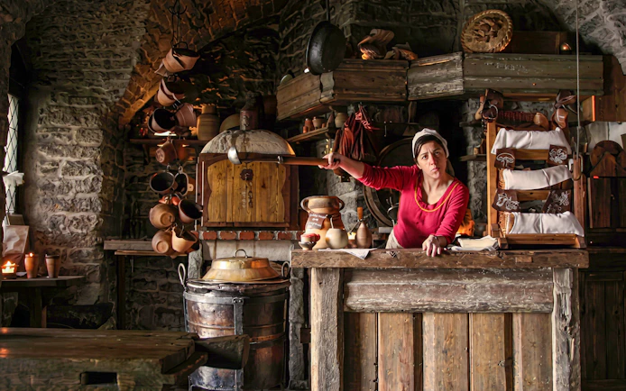 Medieval kitchen in Tallinn with a woman in traditional attire preparing food.