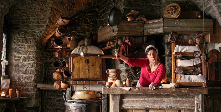 Medieval kitchen in Tallinn with a woman in traditional attire preparing food.