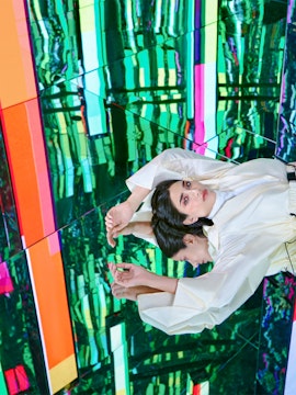 Person in white outfit reflected in colorful mirrored room at AYA Universe.