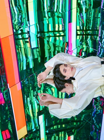 Person in white outfit reflected in colorful mirrored room at AYA Universe.