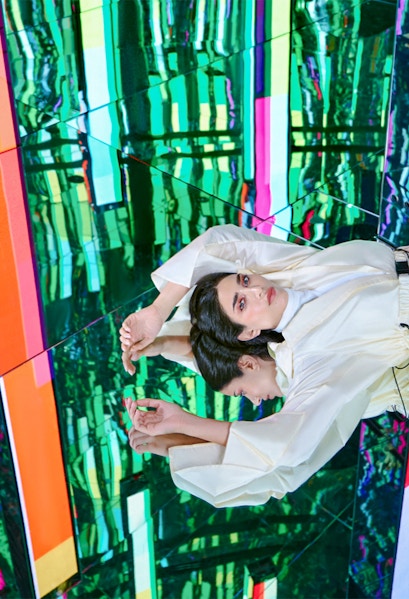Person in white outfit reflected in colorful mirrored room at AYA Universe.