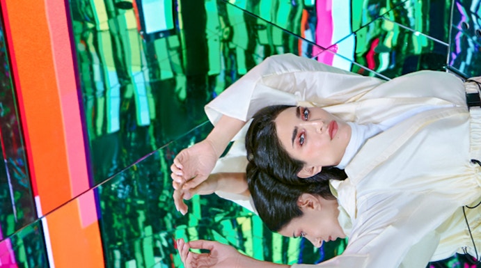 Person in white outfit reflected in colorful mirrored room at AYA Universe.