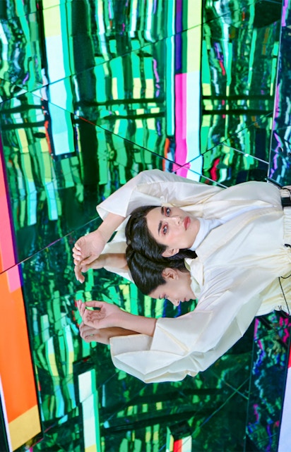 Person in white outfit reflected in colorful mirrored room at AYA Universe.