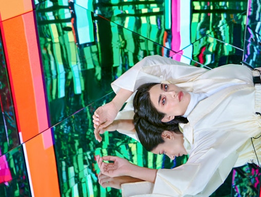Person in white outfit reflected in colorful mirrored room at AYA Universe.