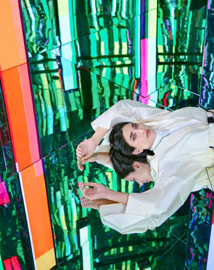 Person in white outfit reflected in colorful mirrored room at AYA Universe.